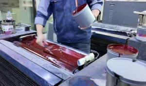 Technician spreading soy-based red ink across the rollers of an offset printing press for sustainable packaging