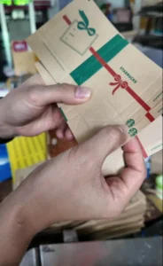 Close-up of hands inspecting Starbucks-branded kraft paper sleeves for registration and fold accuracy